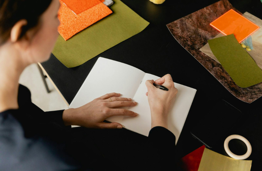 Persona escribiendo en un cuaderno rodeada de muestras de tejidos de colores